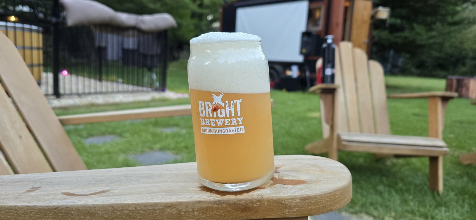 A cold craft beer on the arm of a timber chair in a brewery garden