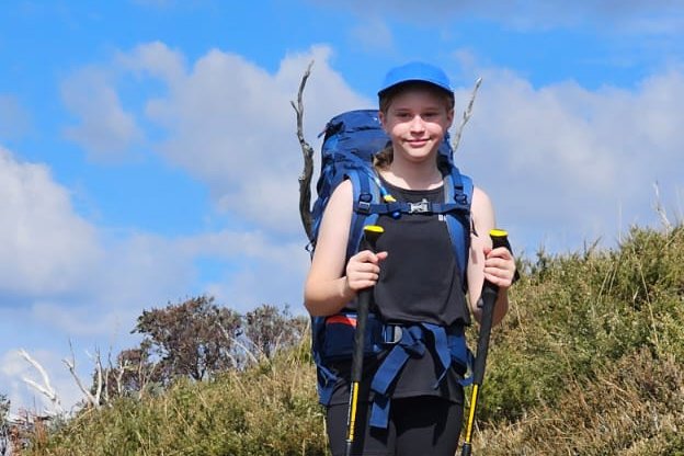 A young hiker with a pack and poles on the ridge track