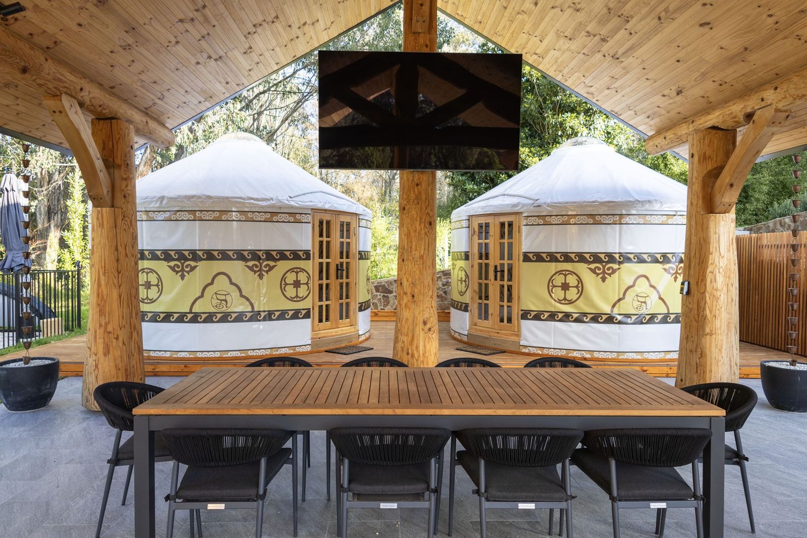 The outdoor dining table under the log pavilion at Bogong Nights glamping, yurts and outdoor TV behind