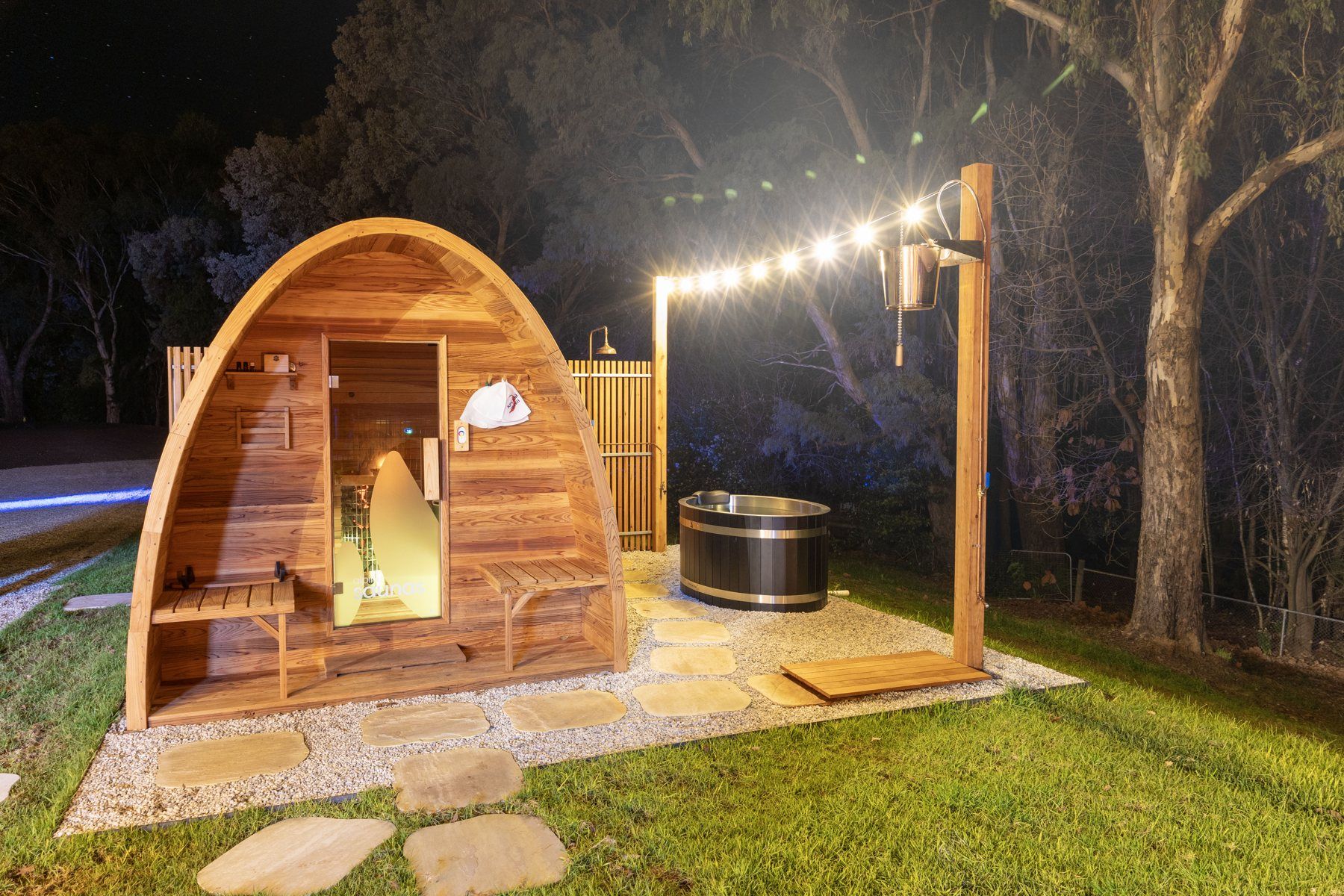 The private sauna at Bogong Nights yurt glamping, Mount Beauty, lit up at night with the ice bath at its door