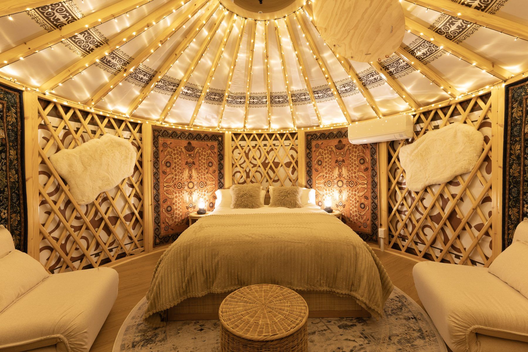 Inside a glamping yurt at Bogong Nights, Mount Beauty, at night: queen bed under the lattice roof, lantern light and rugs