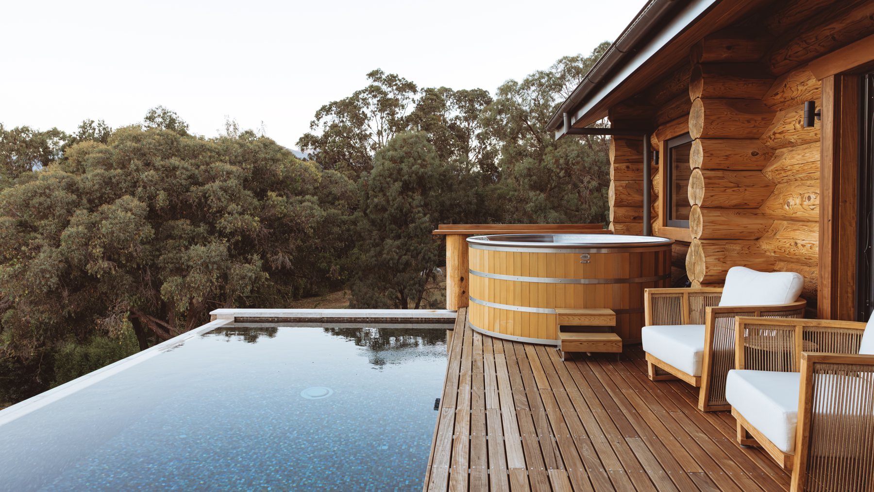 The Log Banya deck near Mount Beauty at dusk: cedar hot tub, infinity pool and the Victorian Alps beyond