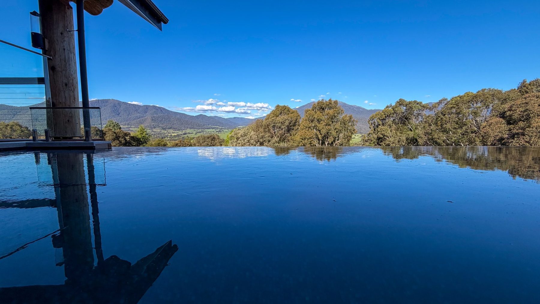 The Log Banya infinity pool by day, mirror-still under a blue sky, Mount Bogong beyond