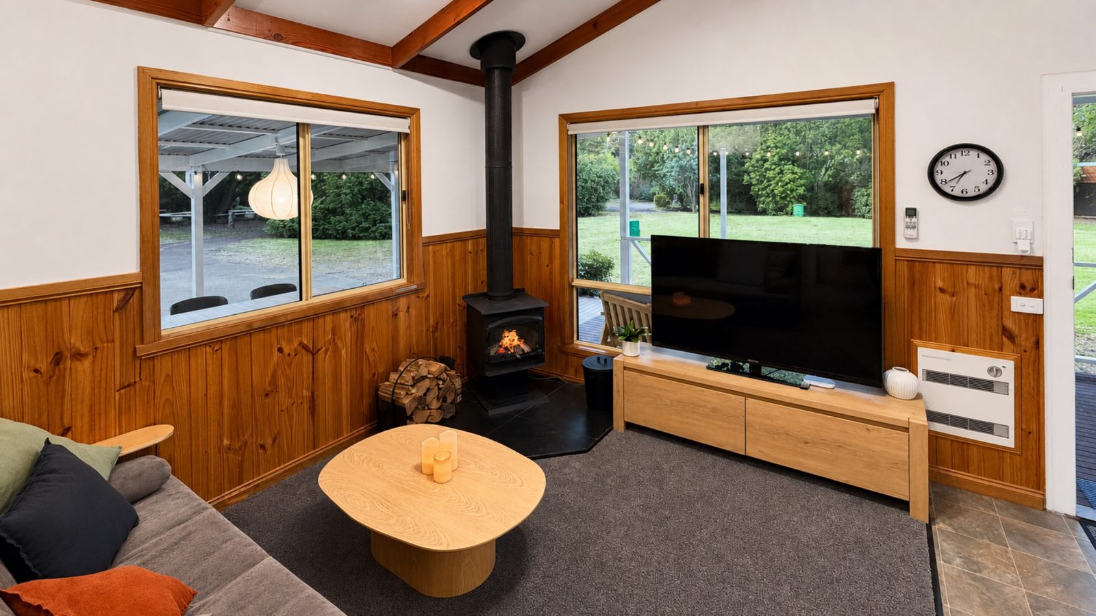 The Cabin's living room in Bright: wood fireplace, sofa and big windows onto the lawn